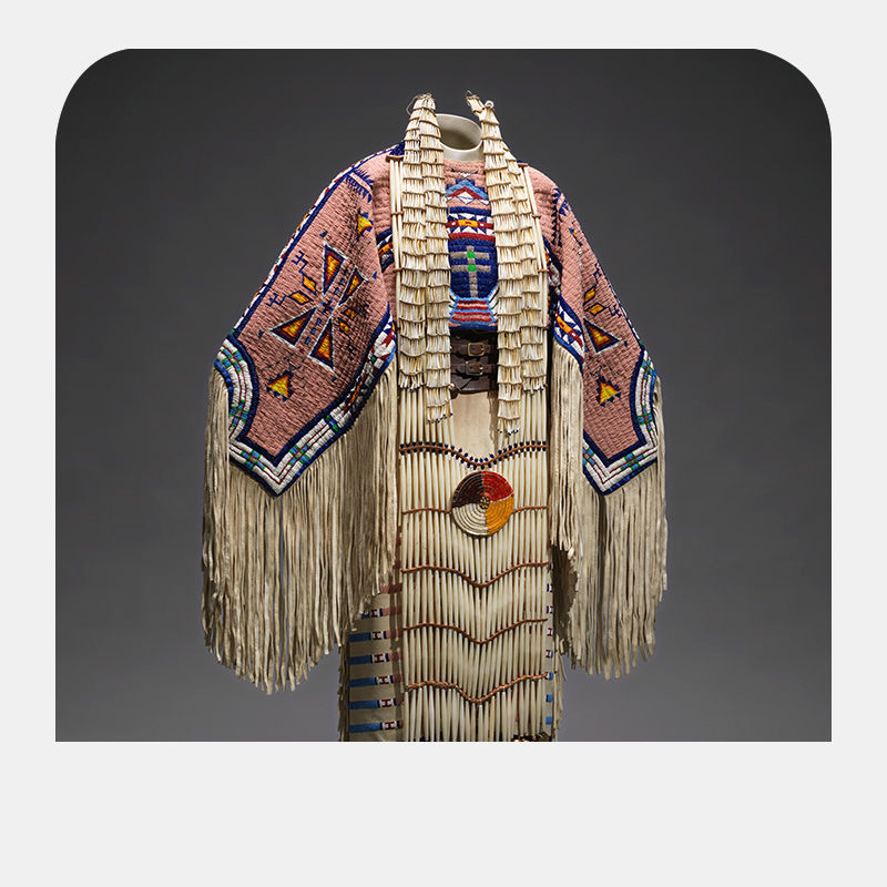 Picture of a dress with pale pink embroidering and various triangular shapes imprinted on the shoulders, the rest hanging like strips of straw towards the ground.